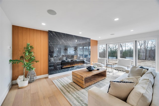 living room featuring a premium fireplace, recessed lighting, baseboards, and wood finished floors