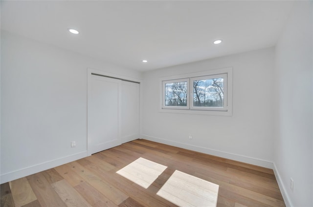 unfurnished bedroom with a closet, recessed lighting, light wood-type flooring, and baseboards