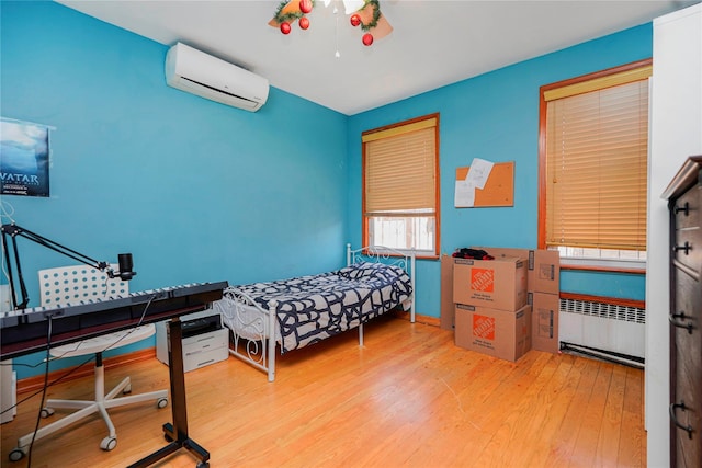 bedroom with wood finished floors, radiator heating unit, and a wall unit AC