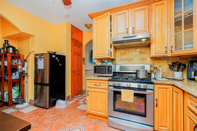 kitchen with glass insert cabinets, under cabinet range hood, decorative backsplash, light tile patterned flooring, and stainless steel appliances