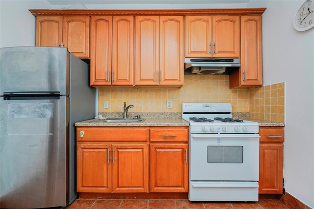 kitchen with white gas stove, a sink, under cabinet range hood, freestanding refrigerator, and light countertops