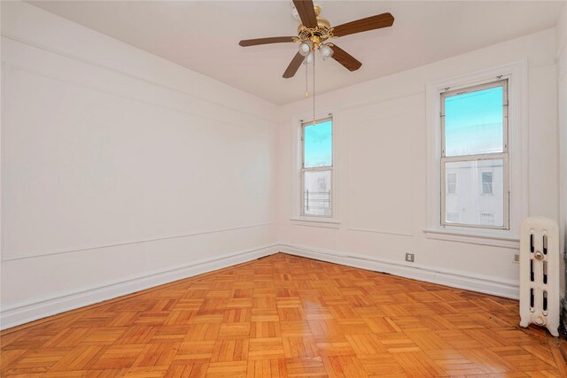 empty room featuring a ceiling fan, radiator heating unit, and baseboards