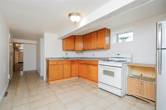 kitchen featuring baseboards, white gas range oven, freestanding refrigerator, brown cabinetry, and a sink