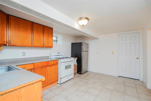 kitchen featuring white gas range, brown cabinets, light countertops, and freestanding refrigerator