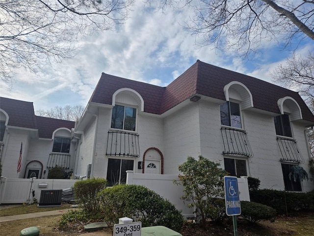 view of front of home featuring central AC unit, mansard roof, fence, and a shingled roof