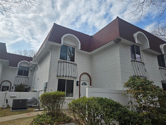 view of front of house with mansard roof, central AC unit, fence, and a shingled roof