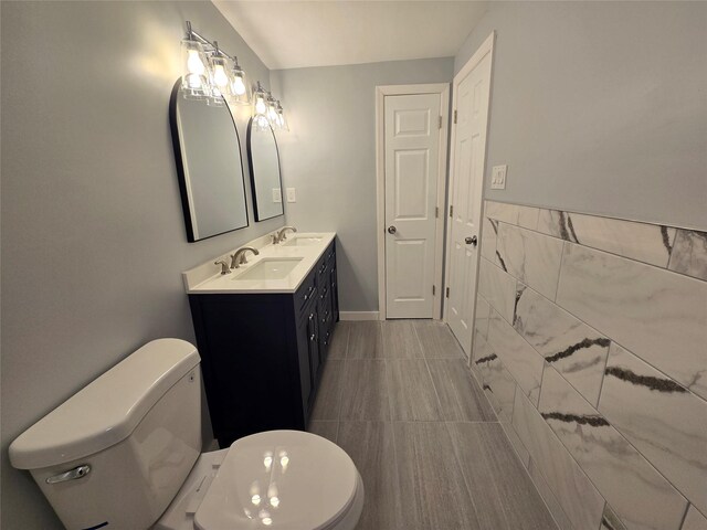 bathroom featuring double vanity, toilet, tile walls, and a sink