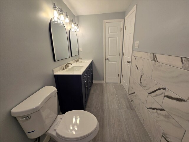 bathroom with double vanity, toilet, tile walls, and a sink