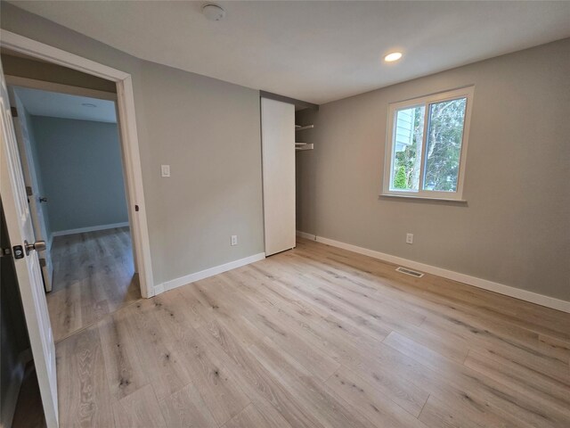 unfurnished bedroom with a closet, visible vents, baseboards, and wood finished floors