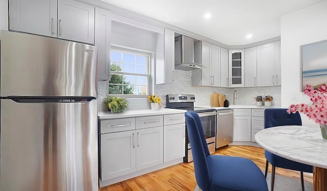 kitchen with decorative backsplash, appliances with stainless steel finishes, light countertops, and wall chimney range hood