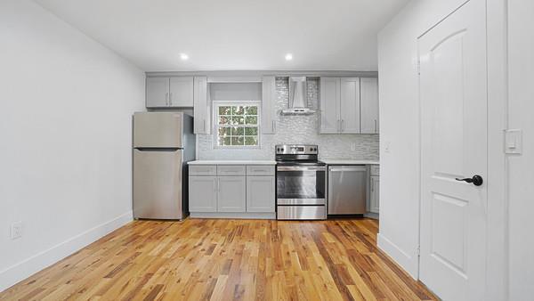 kitchen with decorative backsplash, appliances with stainless steel finishes, light countertops, and wall chimney range hood