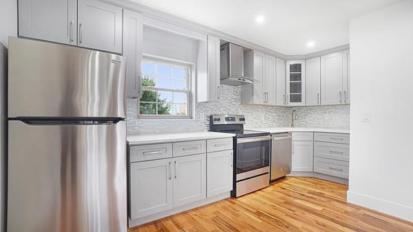 kitchen featuring glass insert cabinets, wall chimney range hood, light wood-type flooring, light countertops, and appliances with stainless steel finishes