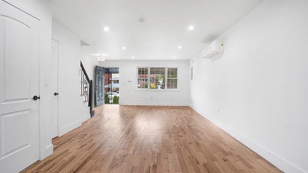 unfurnished living room featuring baseboards, light wood finished floors, recessed lighting, stairs, and a wall mounted air conditioner