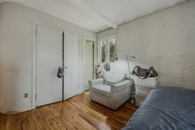 unfurnished bedroom with beam ceiling, wood-type flooring, and a textured wall