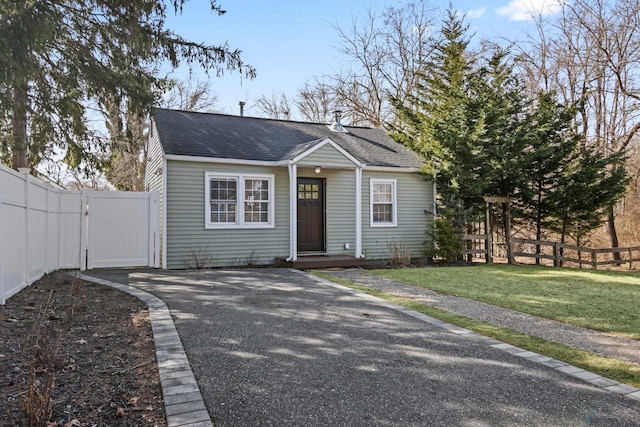 bungalow-style home with a front yard, a gate, fence, and a shingled roof