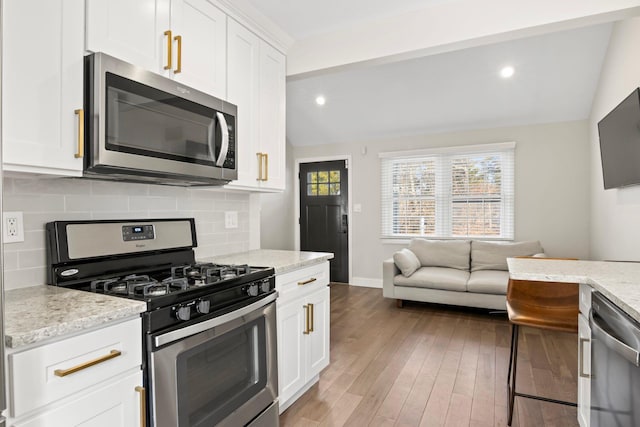 kitchen featuring decorative backsplash, stainless steel appliances, wood finished floors, and vaulted ceiling