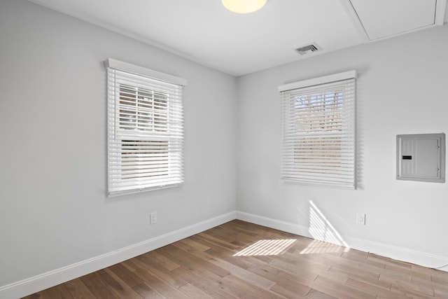 spare room featuring electric panel, visible vents, baseboards, and wood finished floors