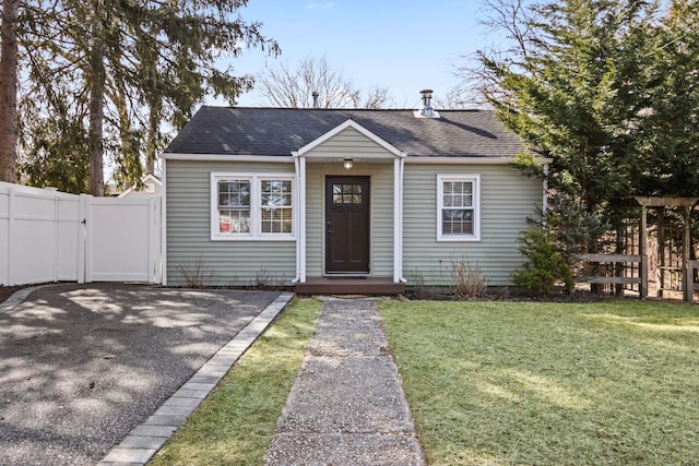 view of front facade featuring a front yard, a gate, fence, and a shingled roof