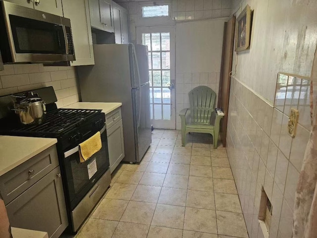 kitchen featuring tile walls, light countertops, light tile patterned floors, gray cabinets, and stainless steel appliances