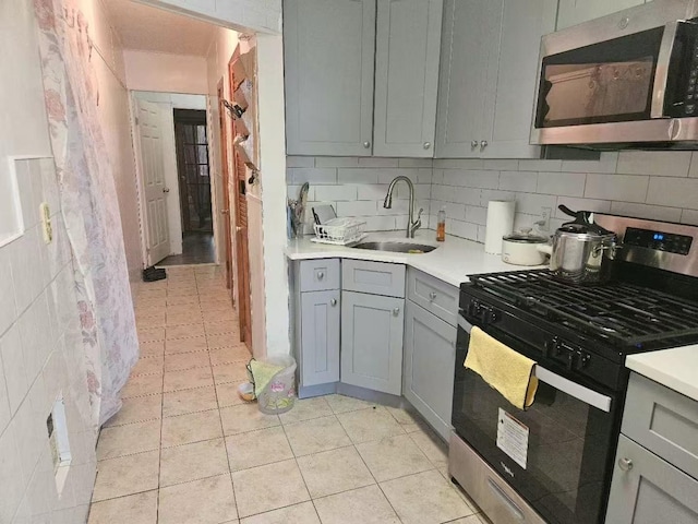 kitchen featuring gray cabinetry, a sink, stainless steel microwave, gas stove, and light countertops