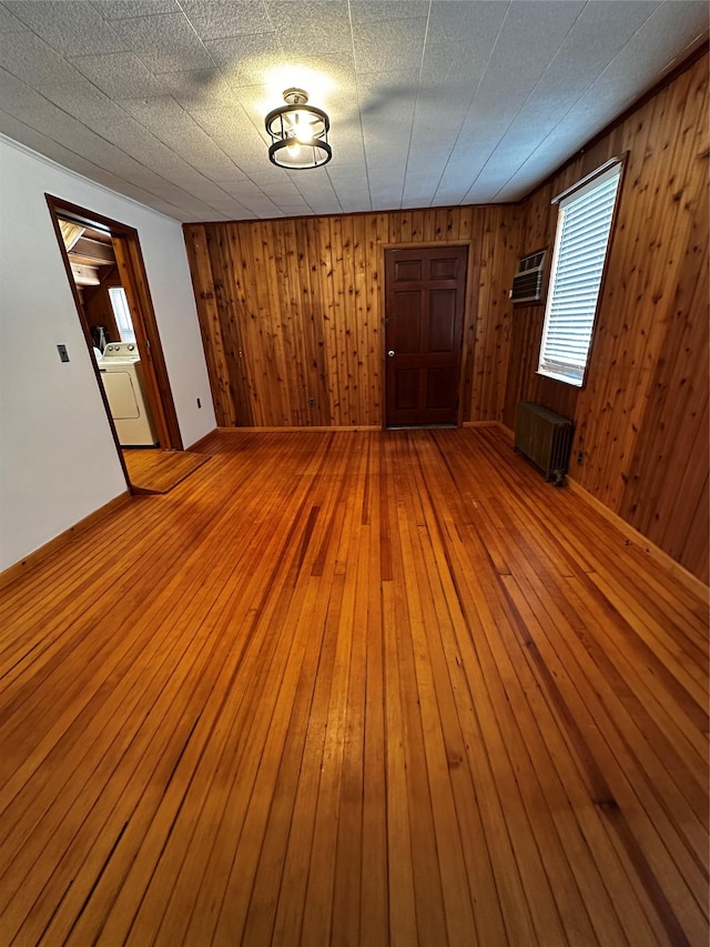 empty room with washer / dryer, light wood-type flooring, radiator heating unit, and wood walls