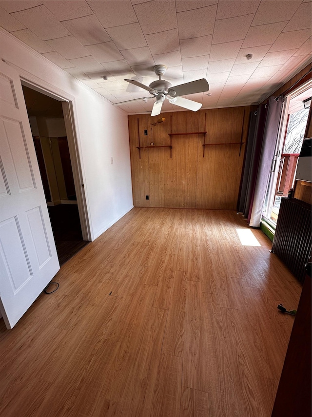 unfurnished living room with wood walls, light wood-type flooring, and a ceiling fan