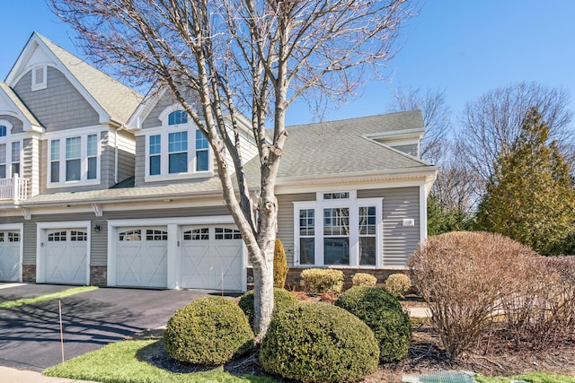 view of front of property featuring aphalt driveway, an attached garage, stone siding, and roof with shingles