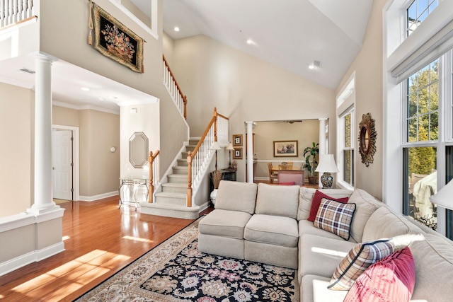 living room featuring baseboards, stairway, wood finished floors, high vaulted ceiling, and ornate columns