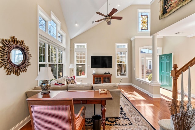 living area with high vaulted ceiling, wood finished floors, decorative columns, baseboards, and stairs