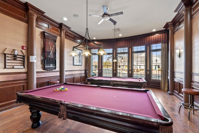 recreation room with hardwood / wood-style floors, a ceiling fan, visible vents, ornamental molding, and wainscoting