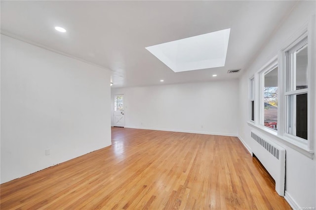 spare room with light wood finished floors, visible vents, radiator heating unit, recessed lighting, and a skylight