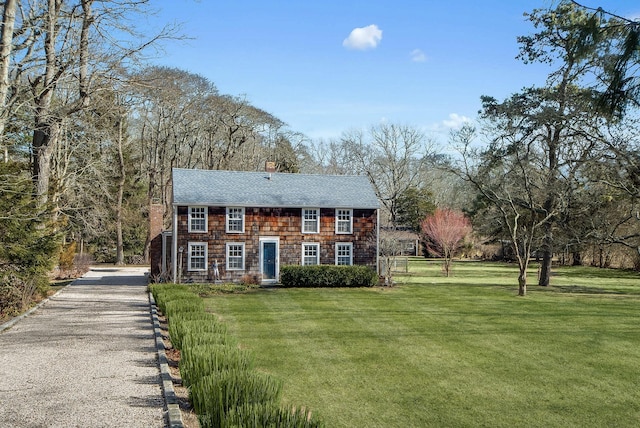 view of front of property featuring a chimney, a shingled roof, gravel driveway, and a front yard