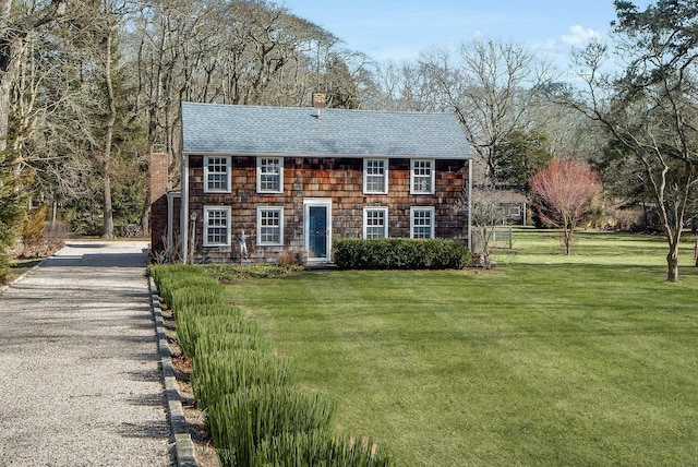 view of front of property featuring driveway, a chimney, a front yard, and a shingled roof