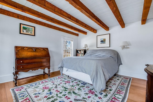 bedroom with beamed ceiling, wood finished floors, and baseboards