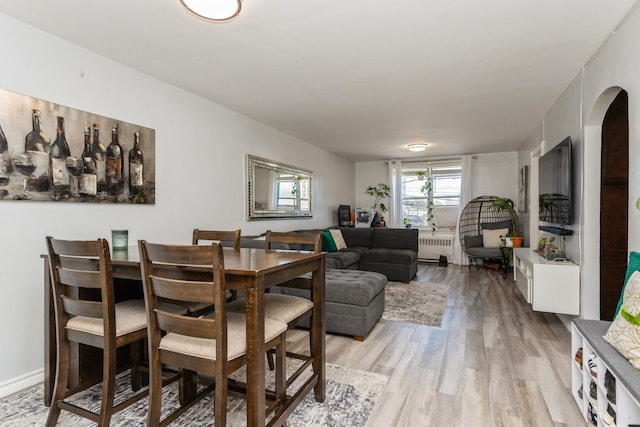 dining space featuring light wood finished floors, radiator, and arched walkways