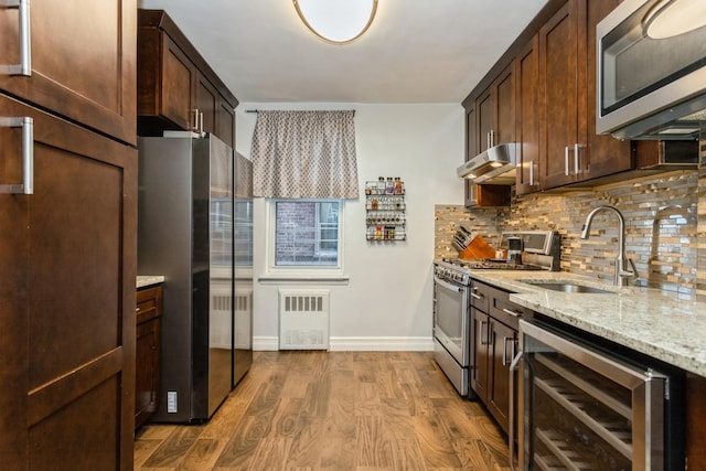 kitchen with under cabinet range hood, a sink, wood finished floors, wine cooler, and appliances with stainless steel finishes