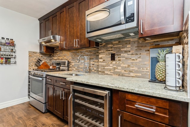 kitchen with beverage cooler, a sink, under cabinet range hood, backsplash, and appliances with stainless steel finishes