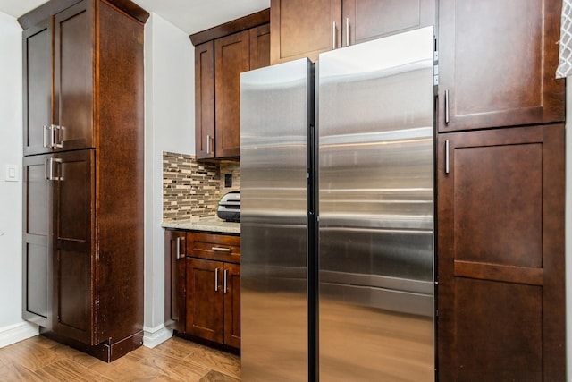 kitchen featuring light stone counters, stainless steel fridge, light wood finished floors, decorative backsplash, and baseboards