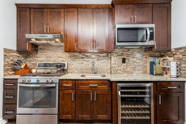 kitchen with beverage cooler, under cabinet range hood, decorative backsplash, appliances with stainless steel finishes, and a sink