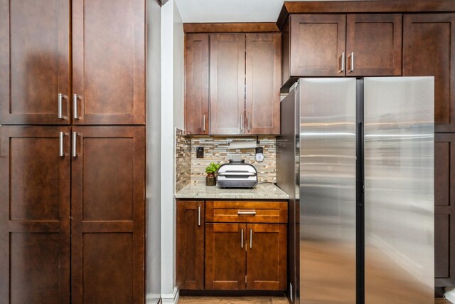 kitchen with light stone counters, backsplash, and freestanding refrigerator