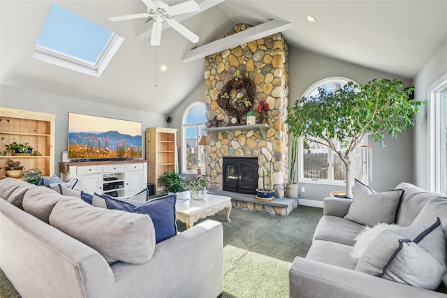 living room with carpet, a stone fireplace, a skylight, high vaulted ceiling, and a ceiling fan