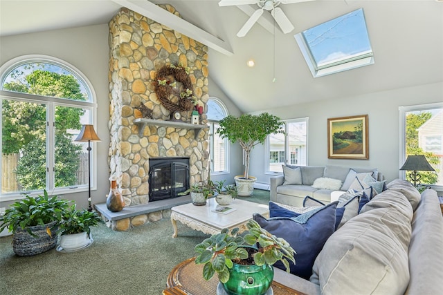 living room with carpet, a skylight, ceiling fan, a stone fireplace, and beamed ceiling