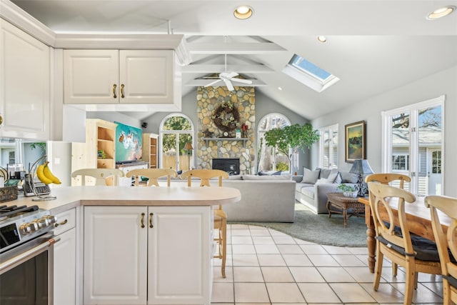 kitchen with lofted ceiling with skylight, stainless steel gas range, light tile patterned floors, a stone fireplace, and white cabinetry