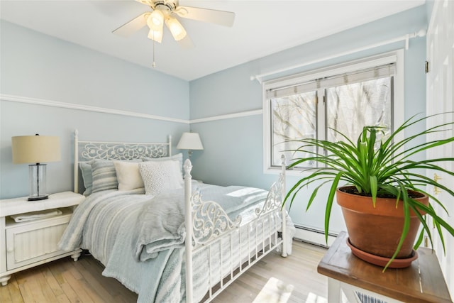 bedroom with ceiling fan, a baseboard heating unit, and wood finished floors