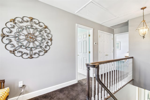 corridor featuring an upstairs landing, attic access, baseboards, and dark colored carpet