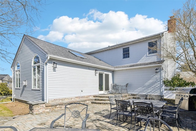 rear view of property featuring outdoor dining space, a patio area, roof with shingles, and a chimney