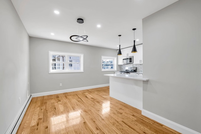 kitchen featuring white cabinetry, stainless steel appliances, decorative backsplash, a baseboard heating unit, and light wood-type flooring