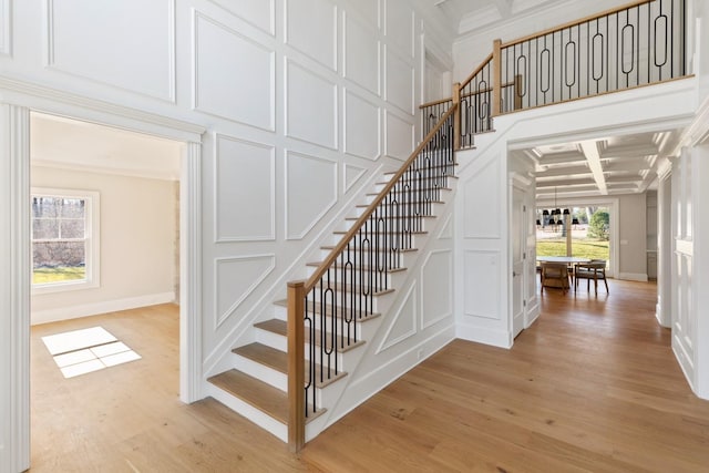 stairway featuring wood finished floors, coffered ceiling, beam ceiling, crown molding, and a decorative wall