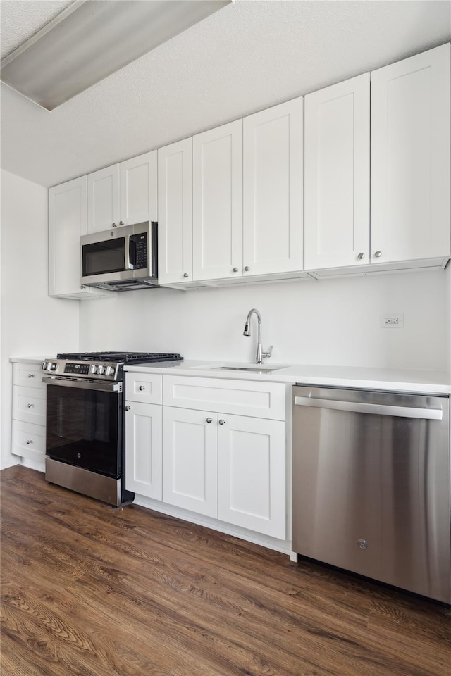 kitchen featuring dark wood-style flooring, appliances with stainless steel finishes, white cabinetry, and a sink