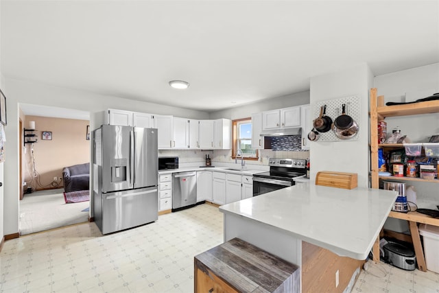kitchen with a peninsula, light countertops, white cabinetry, a sink, and stainless steel appliances
